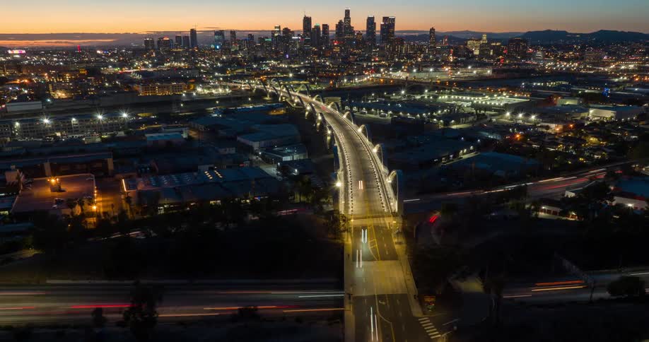 Sixth Street Bridge Viaduct in Los Angeles stretches toward a glowing downtown cityscape at dusk