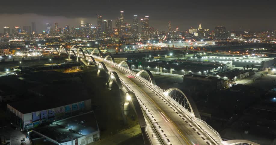 An illuminated Sixth Street Bridge Viaduct in Los Angeles leads into a brightly lit city skyline at night