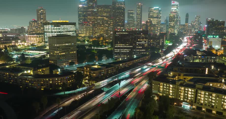 Nighttime Los Angeles traffic blurs into light trails beneath a glowing urban skyline