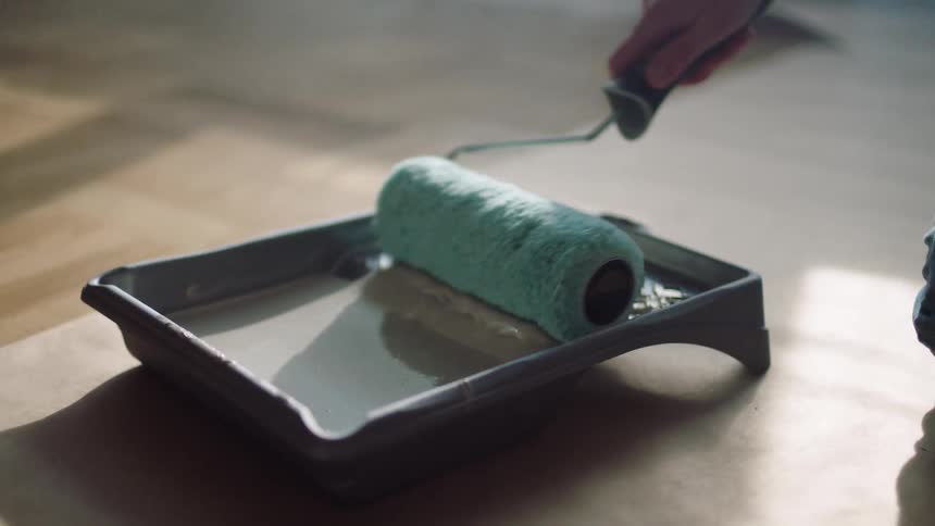 A person is covering their paint brush with grey colored paint