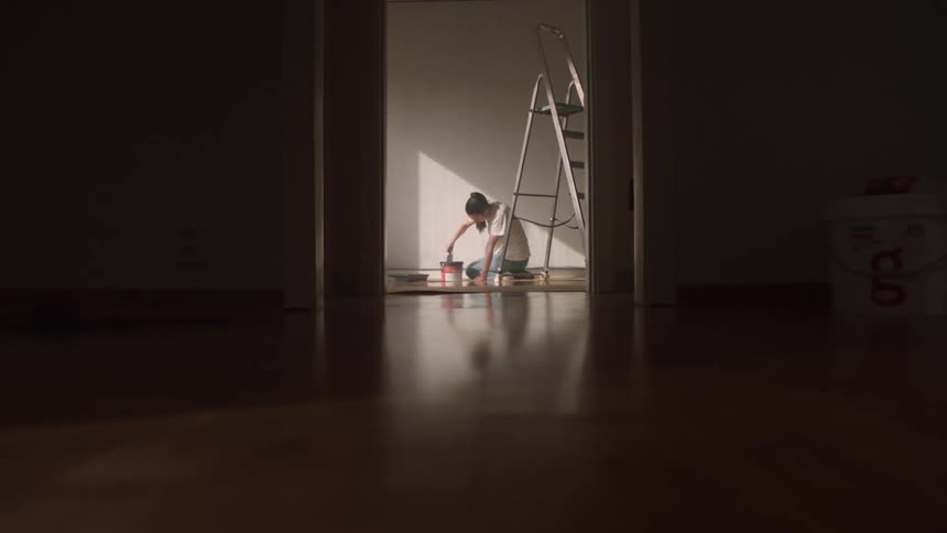 Female painter mixes paint in a container while kneeling in a room during daytime
