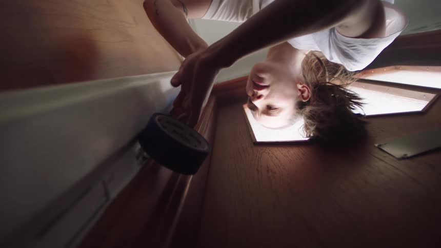 A woman applies masking tape along the edge of a doorway frame