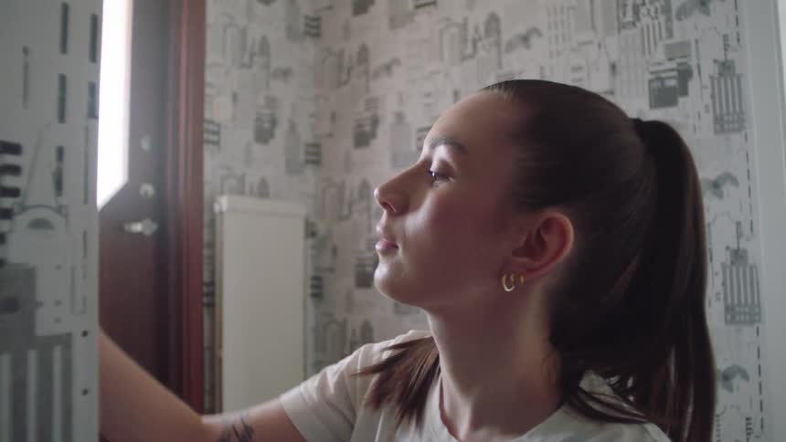 A young female is applying wallpaper in a small room indoors