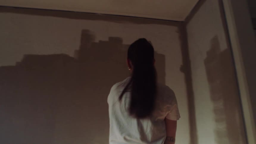 A woman paints a wall in a sunlit room using a roller brush