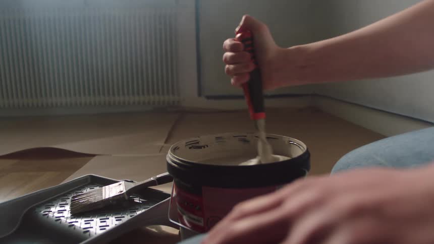 A person is mixing paint in the can
