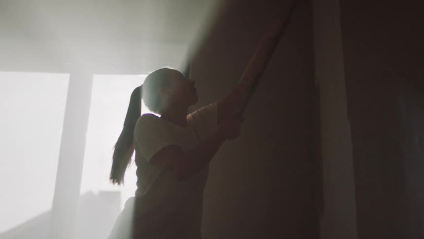 The woman reaches up with the paint roller