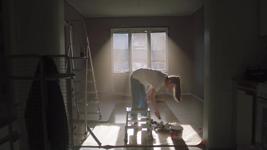 Lady paints a room using a roller and a small ladder in the morning