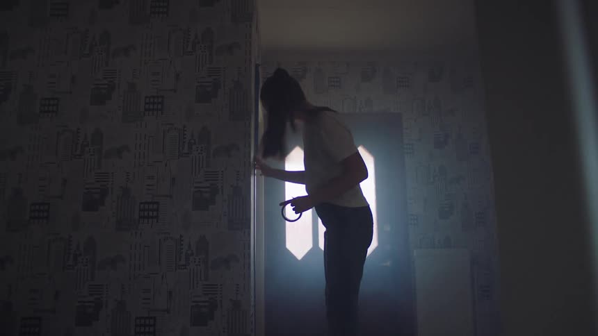 A woman applies cellophane tape to a wall to hold wallpaper in place inside her room at midday