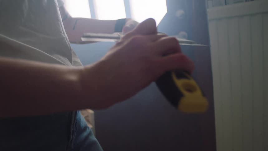 A female painter mixes joint compound paste with a sander during the painting process of a room at midday