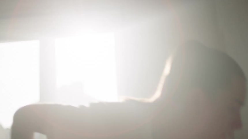 A woman paints a sunlit room with a roller beside a window on a bright day