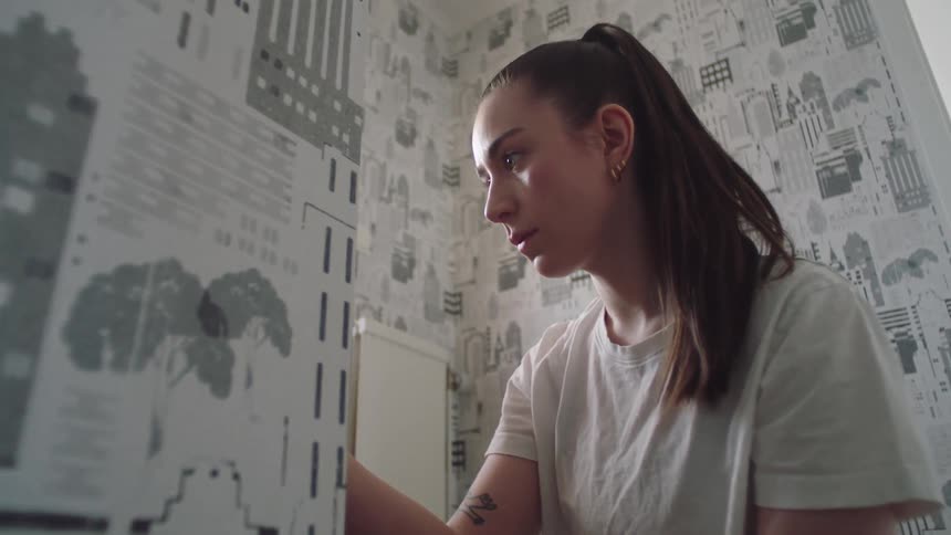 Close up of a young woman applying tape to the interior walls of a home during daytime