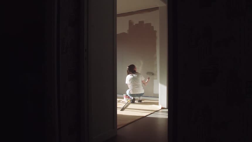 A woman is painting the wall down the hall