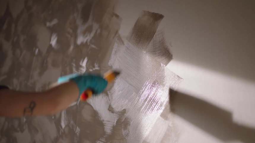 A man paints a room wall with white paint at midday