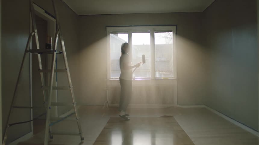 Close up of a female painter walking around a room with a paint roller while inspecting the painted walls