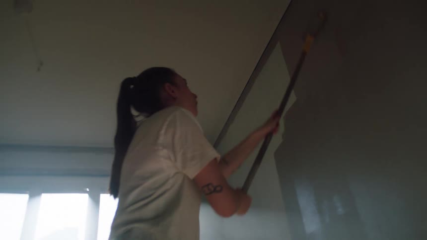 A woman holding a stick with a brush to paint a wall brown color