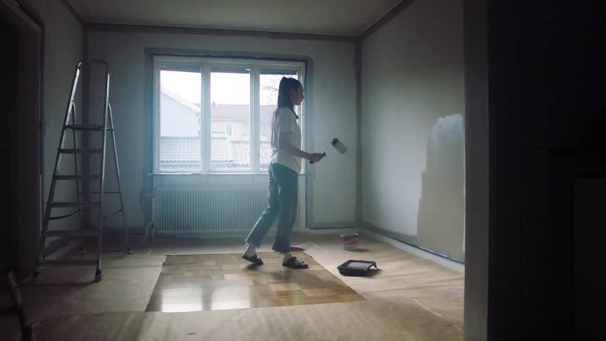 A woman is sitting down as she paints the walls of her house