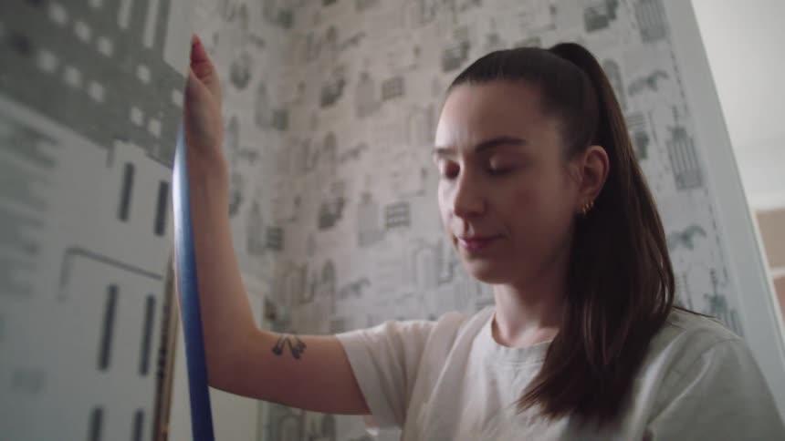 A woman is putting painters tape on the wall