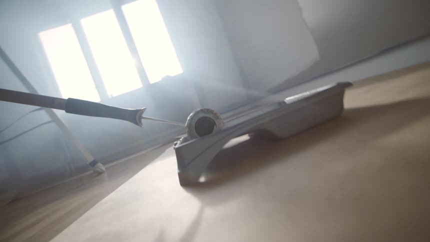 Close up of a paint roller rolled inside a paint tray on the floor in a room