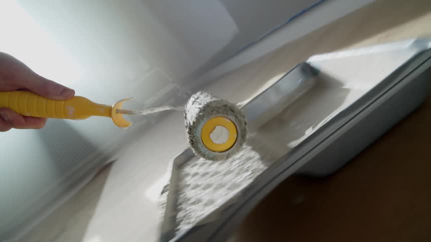 A person covers the roller in paint and begins painting