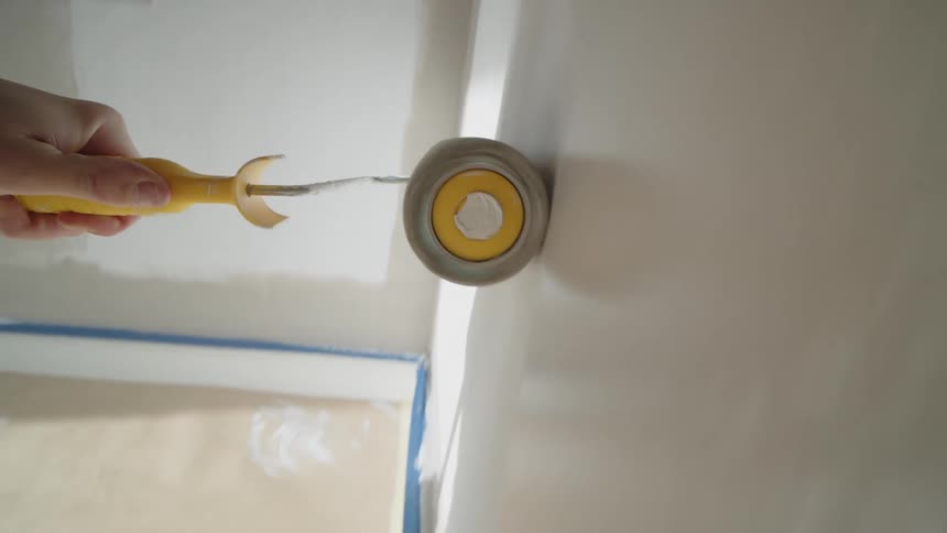 Close up of a persons hand using a paint roller to apply paint on a room wall