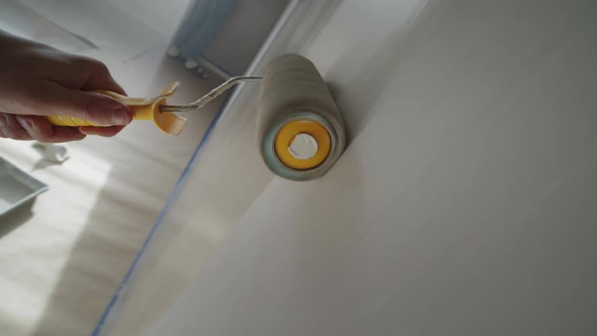 A persons hand holding a round roller brush to paint a wall brown color