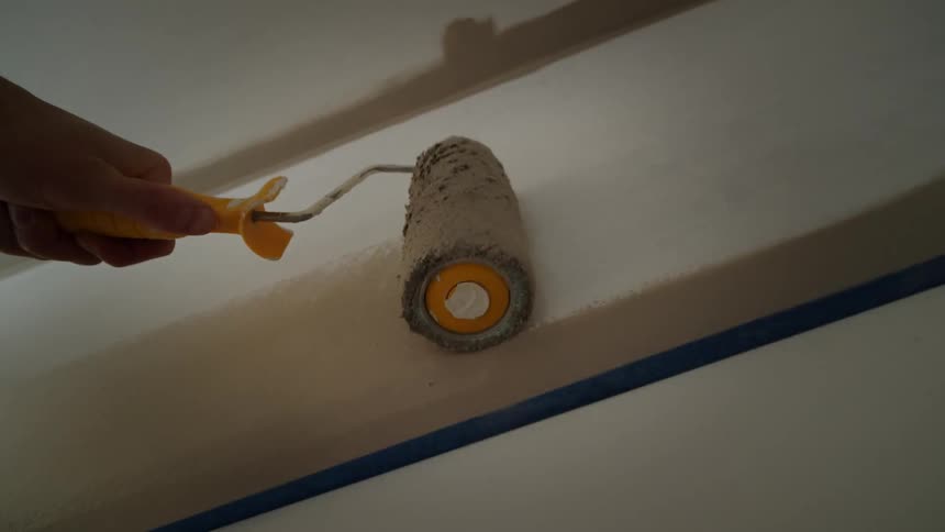 Close up of paint roller used by a person to apply paint on a room wall during daytime