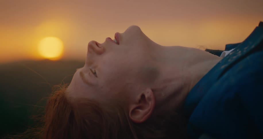 The woman leans back as the sun rises over the field