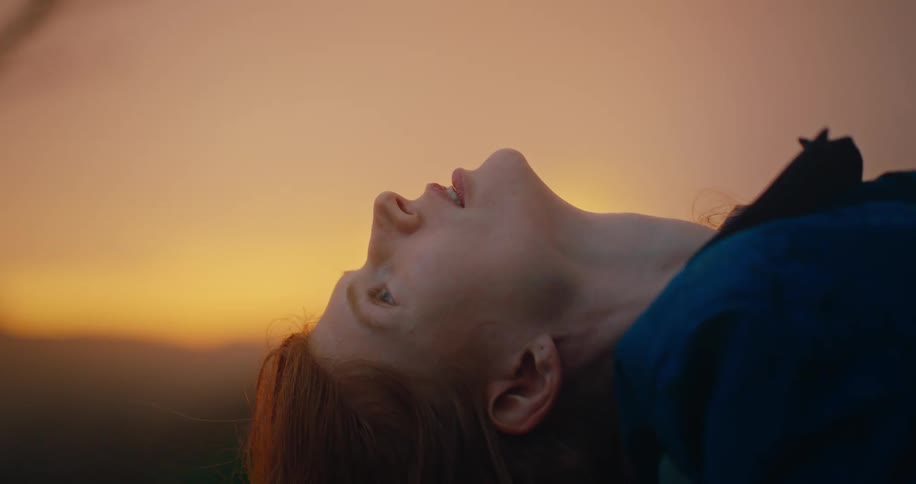 A woman lies on her back outdoors wearing a blue dress at sundown