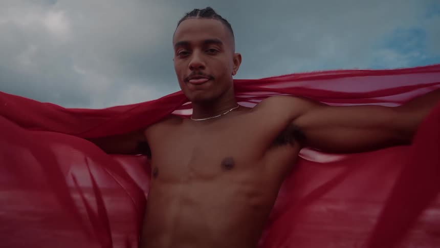 A man has a red sheet around his shoulders on the beach