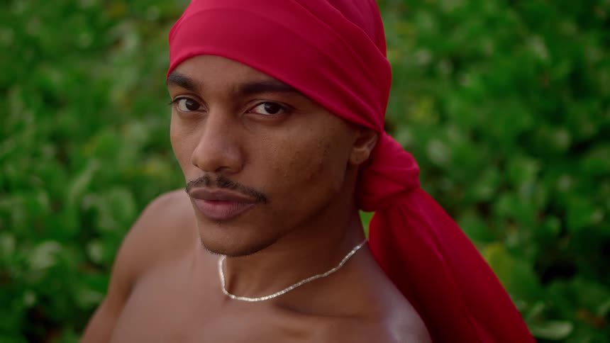 Shirtless man with a red bandana on his head is sitting in an outdoor environment
