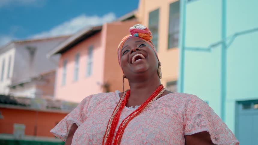 A joyful woman in colorful clothing laughs heartily while standing outside on a bright day