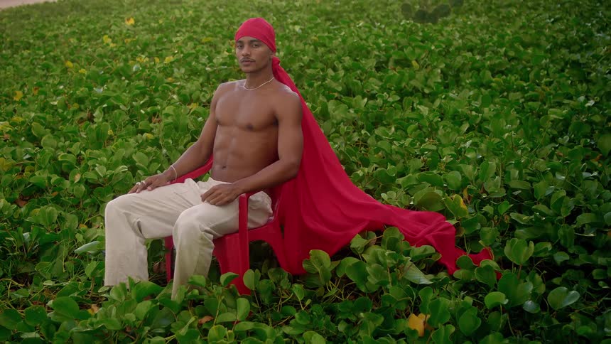 A man is sitting on a red chair wearing a red durag