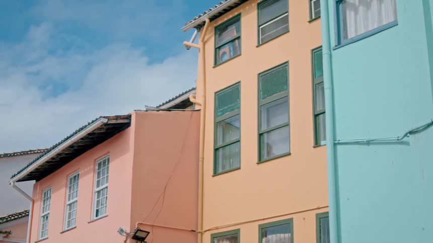 A lowangle view shows a row of colorful residential buildings painted light blue yellow and pink against a partly cloudy sky