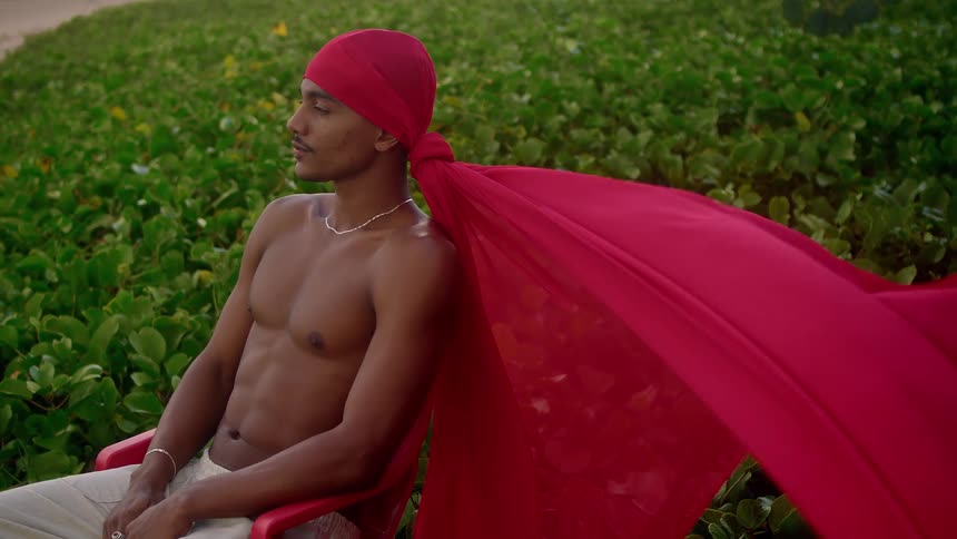 A man sits wearing a red cape tied to his head