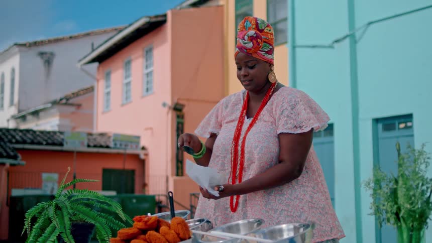 A woman in colorful traditional attire serves food at an outdoor market stall