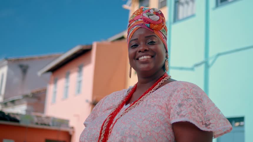A joyful woman in colorful traditional clothing smiles confidently in front of vibrant houses