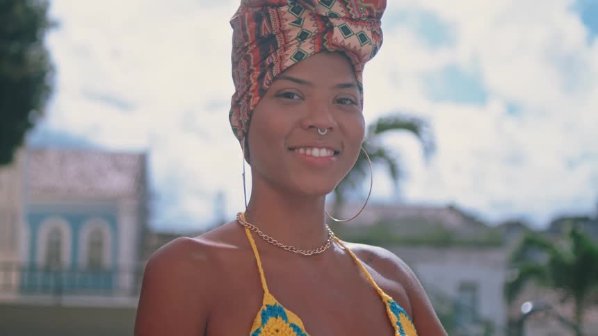 A woman is smiling outdoors in front of a tropical city