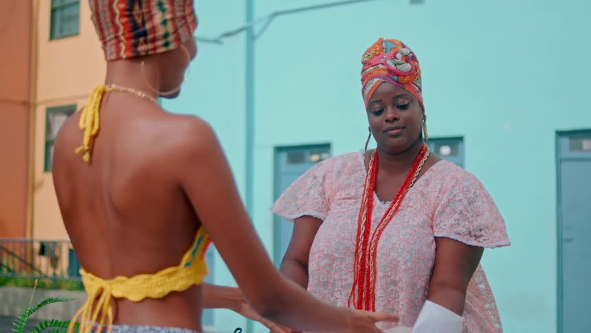A street vendor serves food into a container while interacting with a woman in colorful attire
