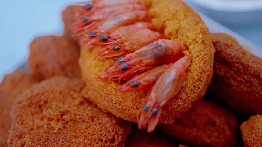 A closeup shot highlights a traditional acaraj a goldenbrown fritter with whole pink shrimp embedded in the top crust