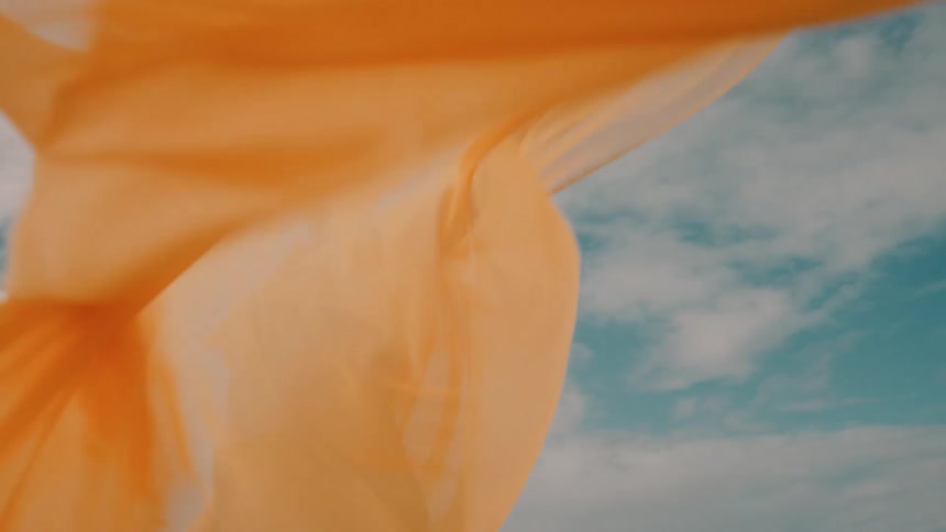 Smiling woman poses confidently in yellow outfit under bright cloudy sky
