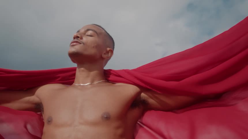 A man lifts a red blanket and wraps it around himself