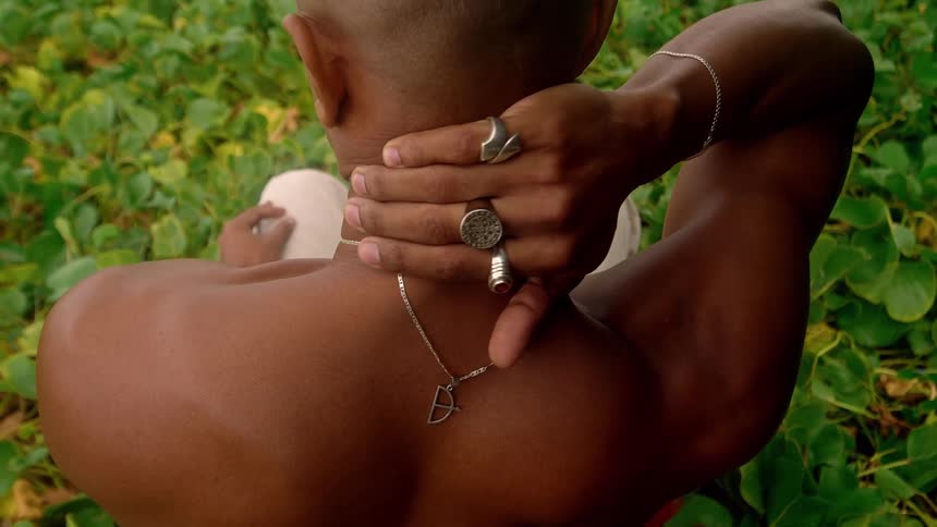 A man sits on the ground and rubs the back of his neck