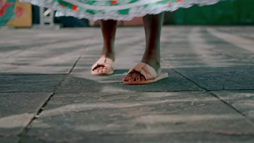 Dancing legs of a black female in gown and pink sandal at midday