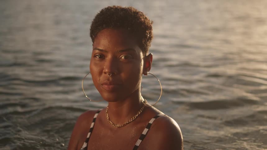 A woman is smiling in ocean water as the sun is setting