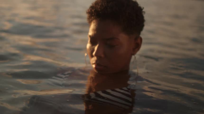 The face of a young woman wearing huge golden earrings who is standing with her body in the water and only her head sticking out