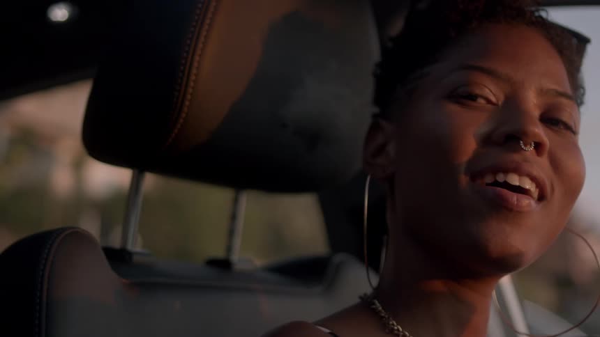 A black woman is singing in her car moving along with the music
