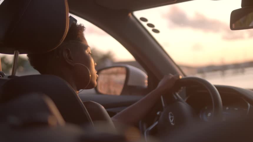 A woman is driving her vehicle during dusk as the sun sets