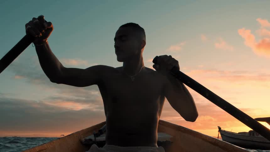 Man is rowing a boat on the ocean while the sun is setting