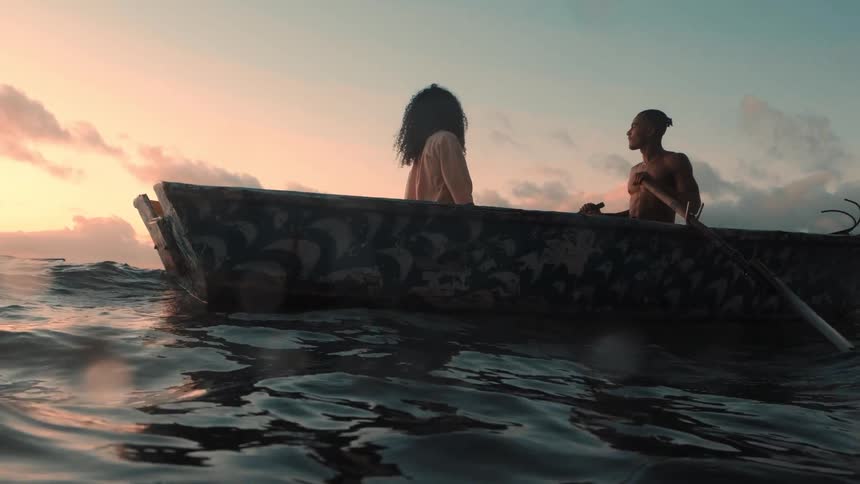 Man and woman sit in a rowboat looking towards the sun sitting on a red horizon