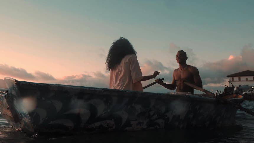 A man and a woman in a canoe enjoy a pleasant time together at sundown with the shirtless man paddling as they glide across the water
